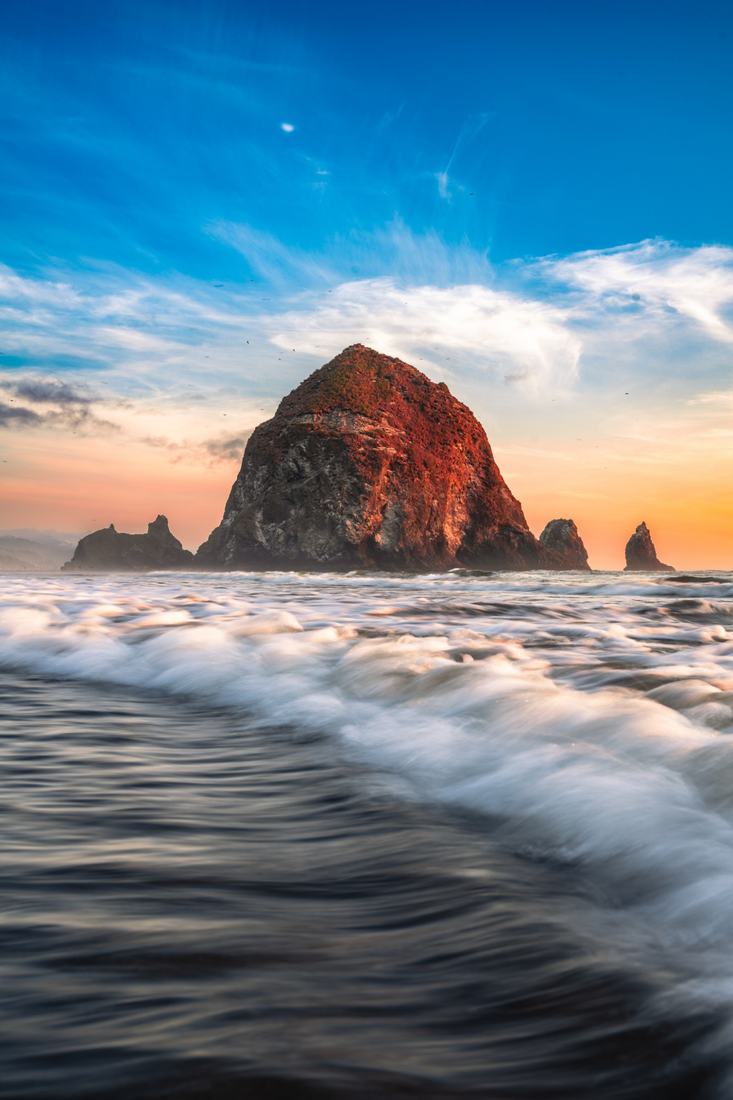 Long-exposure surf sweeping toward Haystack Rock under a blue evening sky