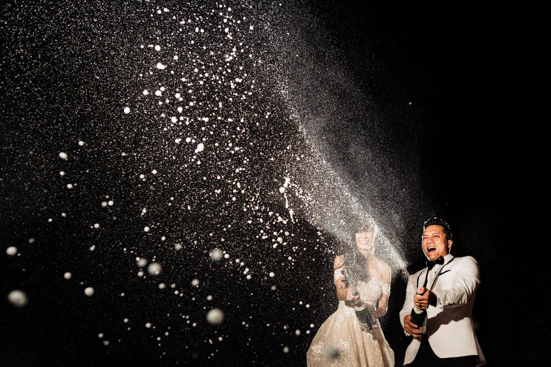 Bride and groom laughing as they spray champagne into the night air