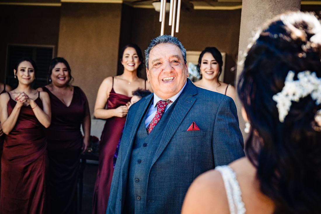 Father beaming as he sees his daughter in her wedding dress for the first time, bridesmaids tearing up behind him